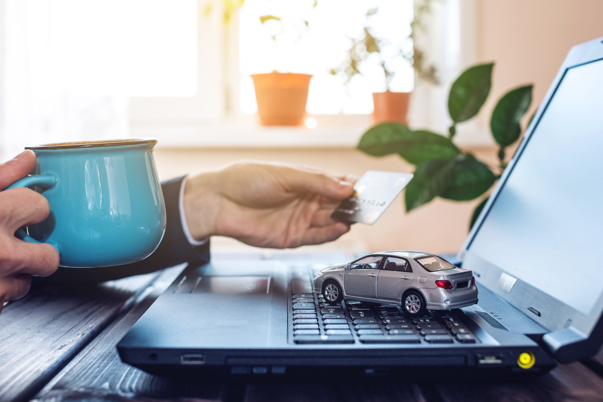 Homme dans le costume de travail au bureau à un ordinateur portable, tenant une voiture payant avec une carte de crédit
