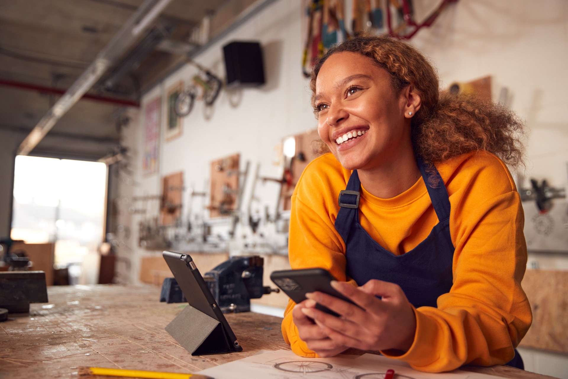 Propriétaire d’entreprise femelle dans l’atelier utilisant la tablette numérique et retenant le téléphone mobile